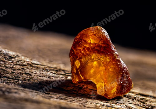 Preview: Natural amber. A piece of yellow transparent natural amber on large piece of dark stoned wood.