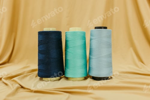 Preview: Close-up shot of three spools of different colored thread on a beige cloth