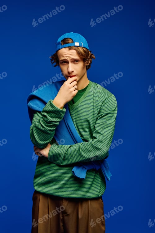 Preview: Trendy young man showcases modern style in vibrant blue backdrop during studio shoot