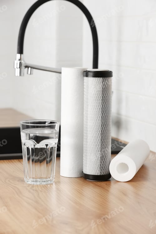 Preview: A glass of clean fresh water and set of filter cartridges on wooden table in a kitchen interior.