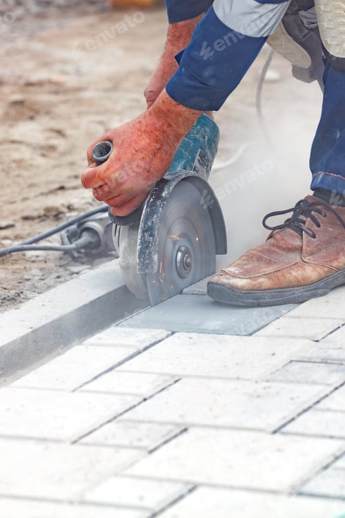 Preview: Vertical closeup of the builder's hands cutting paving slabs with a grinder and a diamond saw.