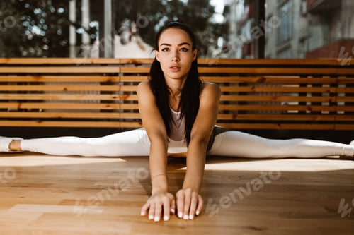 Preview: Beautiful slender dark-haired girl dressed in white sports top and tights is doing the splits in the