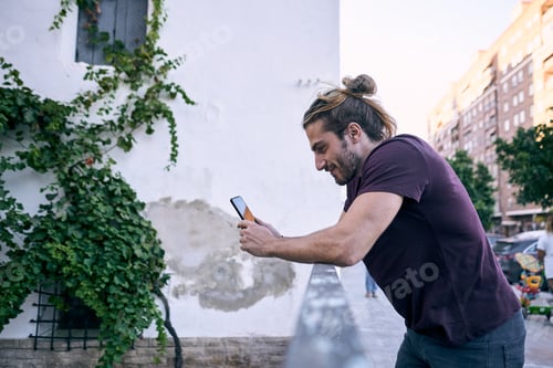 Preview: caucasian guy standing calm and relaxed with the smartphone in his hands smiling leaning on the