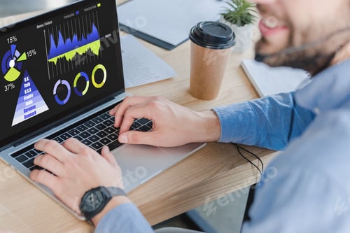 Preview: cropped shot of smiling businessman in headset using laptop with business charts on screen