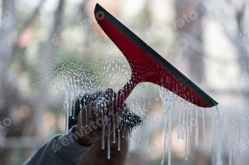 Preview: Closeup of a person cleaning windows with a red squeegee under the lights with a blurry background