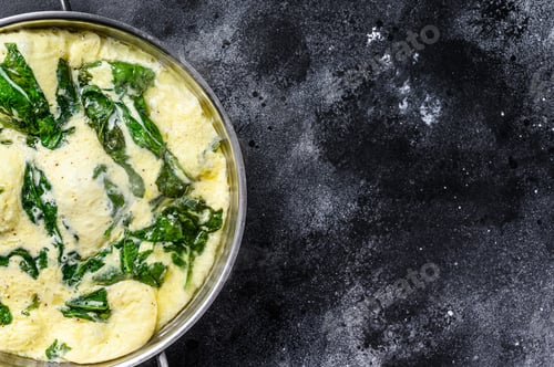 Preview: scrambled eggs with spinach and Parmesan cheese. Black background. Top view. Copy space