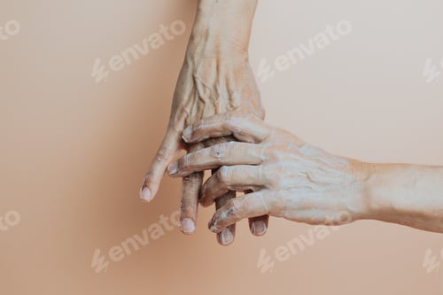 Preview: Two old hands using body lotion. Self care and cosmetics. Pastel colour background, minimalism.