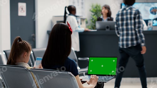 Preview: Mother and little girl using laptop with greenscreen in waiting room