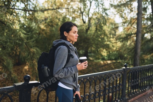 Preview: A brunette girl in a hoodie in nature walks in the Park in autumn weather with coffe cup of paper