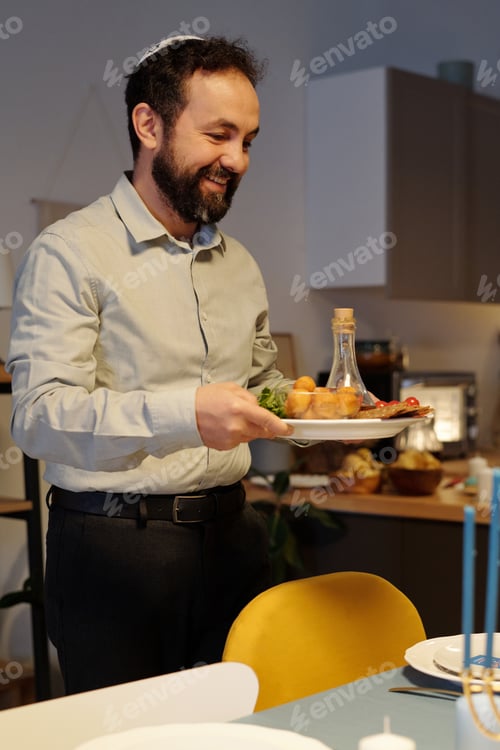 Preview: Smiling bearded man holding plate with bottle of oil and homemade snacks