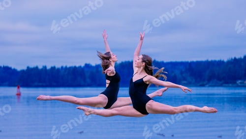 Preview: Two dancers perform a synchronized leap over a lake at twilight with forest in the background, USA
