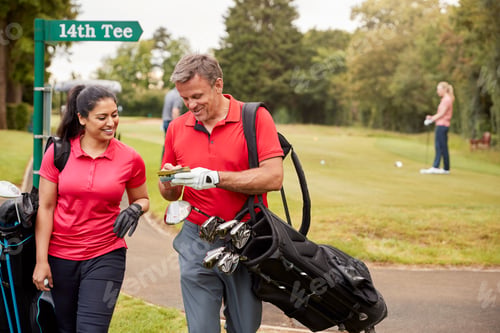 Aperçu: Mature Couple Playing Round Of Golf Carrying Golf Bags And Marking Scorecard