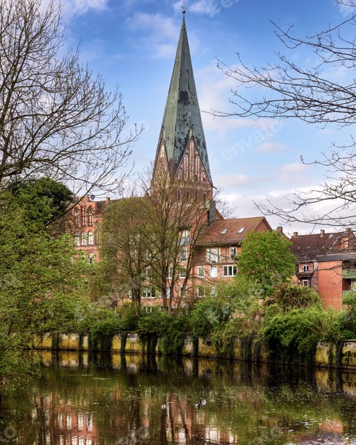 Preview: Vertical shot of the bell tower of St. John's Church and riverfront buildings in Lueneburg, Germany