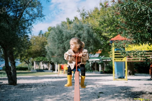Preview: Little girl sits on a swing balancer holding the handle and looks to the side