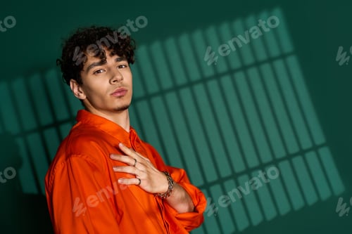 Preview: Curly-haired man in stylish outfit poses confidently in trendy studio space