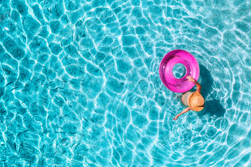 Preview: Aerial view of a young woman in hat swimming with pink swim ring