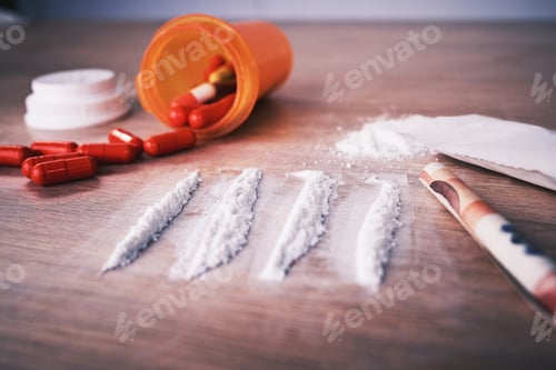 Preview: Lines of cocaine, an open bottle of pills and paper money bent into a roll on a wooden table. Cocai