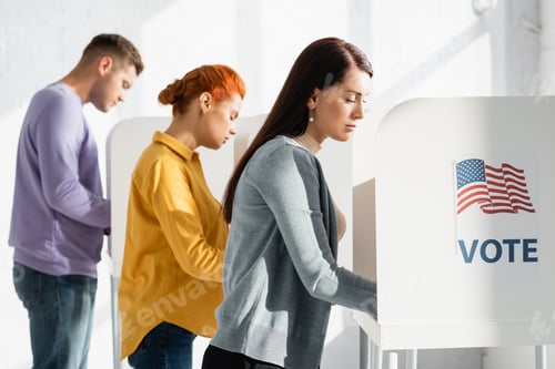 Preview: voters in polling cabins with american flag and vote lettering on blurred background