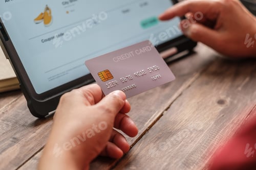 Preview: close up woman hand using credit card shopping online on mobile app on wood table at home