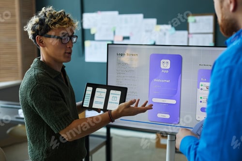 Preview: Young Adult Caucasian Man Presenting Mobile App Design to Colleague in Office