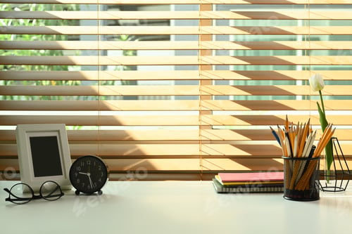 Preview: Creative workplace with picture frame, eyeglasses, notebooks and pencil holder on white table.