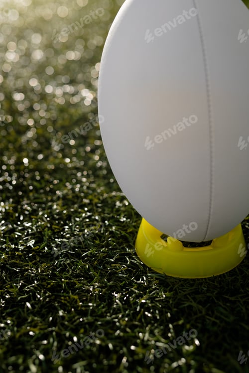 Preview: White rugby ball in yellow stand over grass with copy space, in slow motion