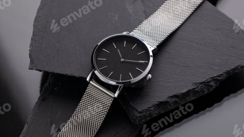 Preview: Top view of a fashionable minimalistic stainless steel wristwatch on flat black stones in the studio