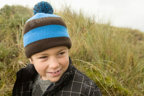 Preview: Young boy smiling in a striped beanie on a cloudy day in the outdoors