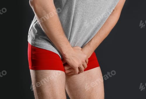 Preview: Man suffering from pain on black background, closeup. Urology problems