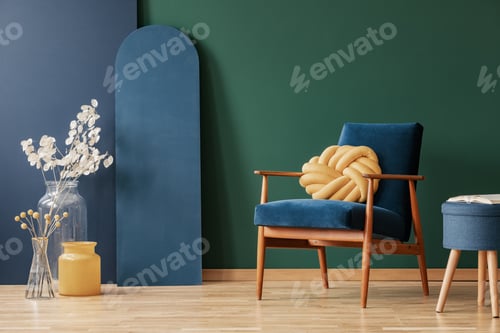 Preview: Yellow pillow on wooden armchair in blue and green flat interior with flowers and stool. Real photo