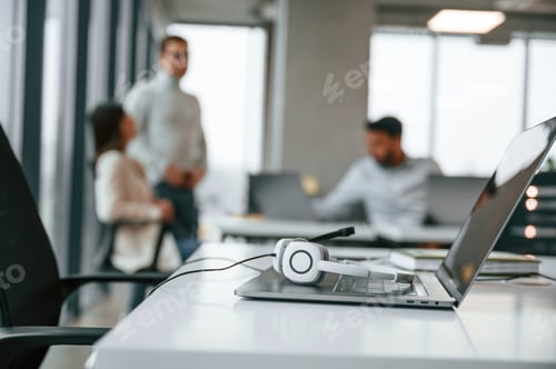 Preview: Headphones is lying down on the laptop. Men and woman are working in the office together