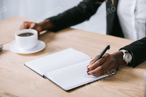 Preview: cropped view of african american woman with notebook and cup of coffee