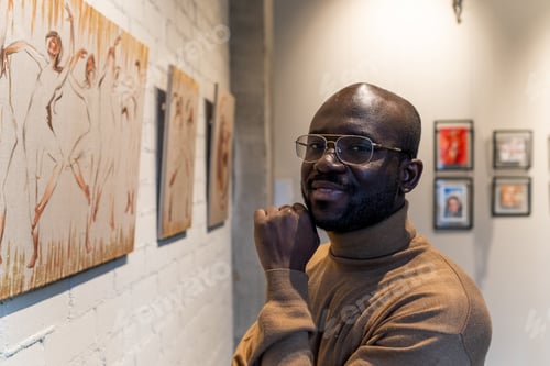 Preview: Happy young African man looking at you while standing by wall with artworks