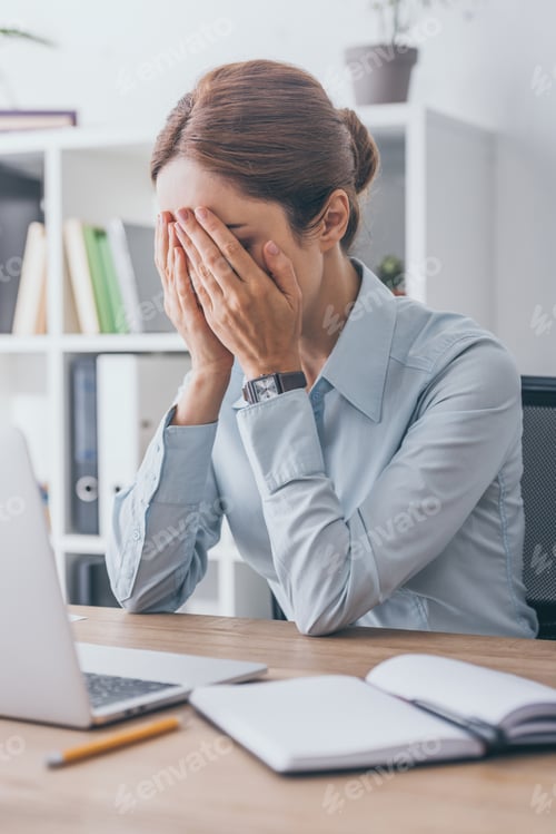 Preview: stressed adult businesswoman covering face with hands at workplace