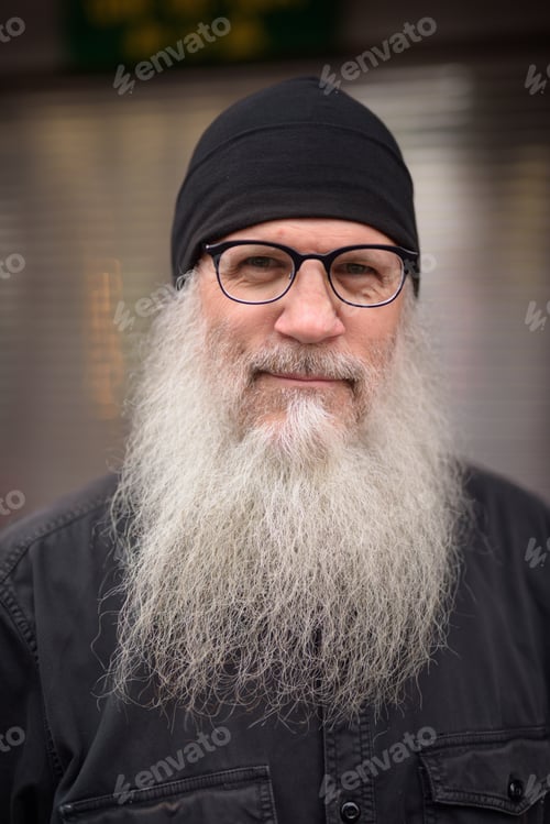 Preview: Face of mature handsome bearded man with eyeglasses in the streets outdoors