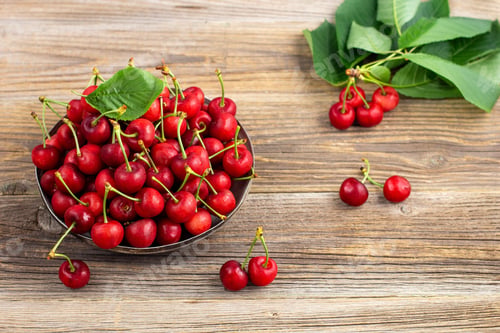 Preview: Ripe sweet cherries with green leaves in a metal plate on wooden background