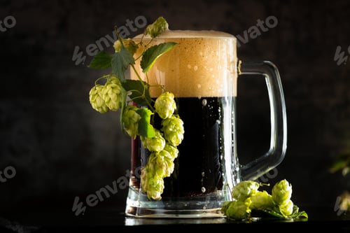 Preview: Glass of dark beer with hops around on a dark background