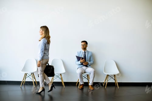 Preview: Businesswoman with suitcase passing by young man sitting at chair