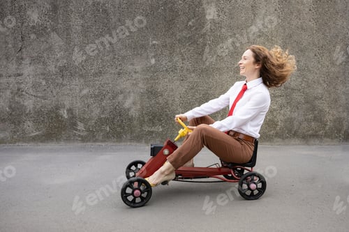 Preview: Funny businesswoman driving retro pedal car outdoor