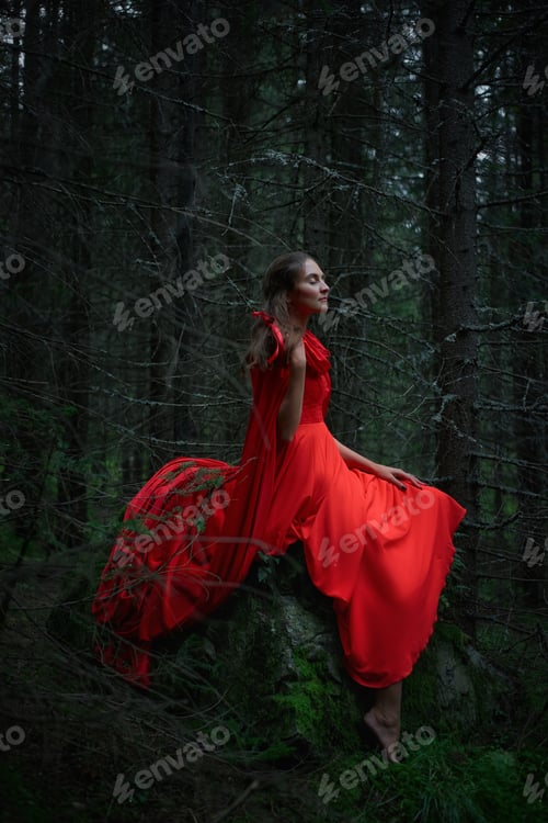 Preview: Woman sits on a rock in a forest wearing a red dress during twilight hours