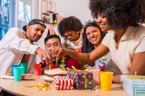 Preview: Multi-ethnic group of friends at a birthday party in a home setting, placing the candles on the cake