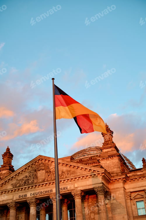 Preview: German flag waving in front of historic building under a vibrant evening sky. Berlin, Germany
