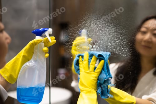 Preview: Cleaning service concept. Close up of female hands in yellow gloves cleaning mirror