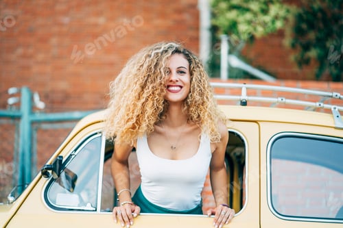 Preview: Portrait of happy blond woman leaning out of window of classic car