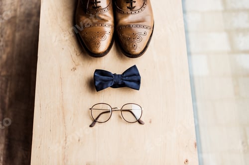 Preview: high angle view of shoes, tie bow and glasses on wooden stand