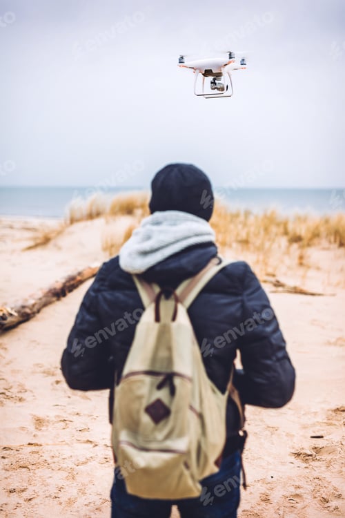 Preview: Man operating a drone while trekking on beach