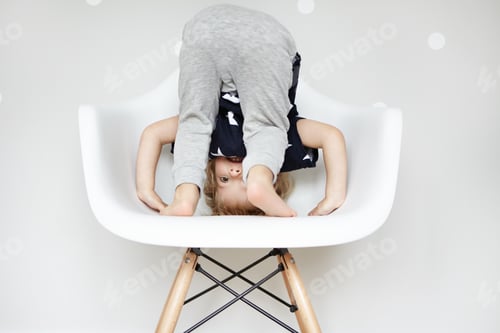 Preview: Studio portrait of playful cheerful two-year old child with blonde hair, doing somersault with his h