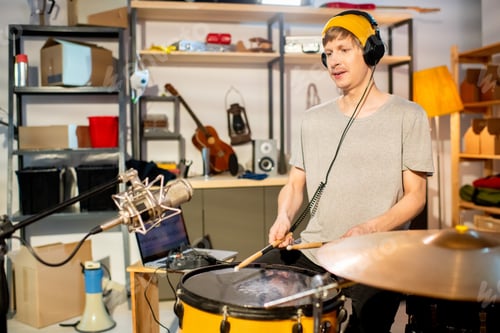 Preview: Young drummer with headphones beating drum with drumsticks during rehearsal