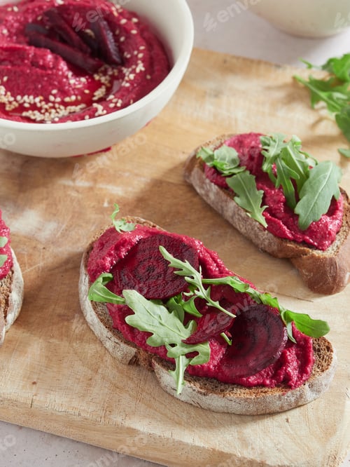 Preview: close-up view of beet root hummus bruschetta with rocket leaves on wooden cutting board