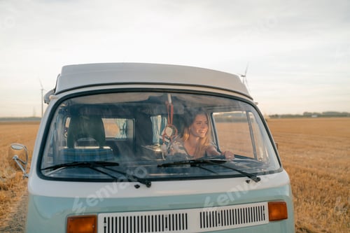 Preview: Smiling young woman driving camper van in rural landscape